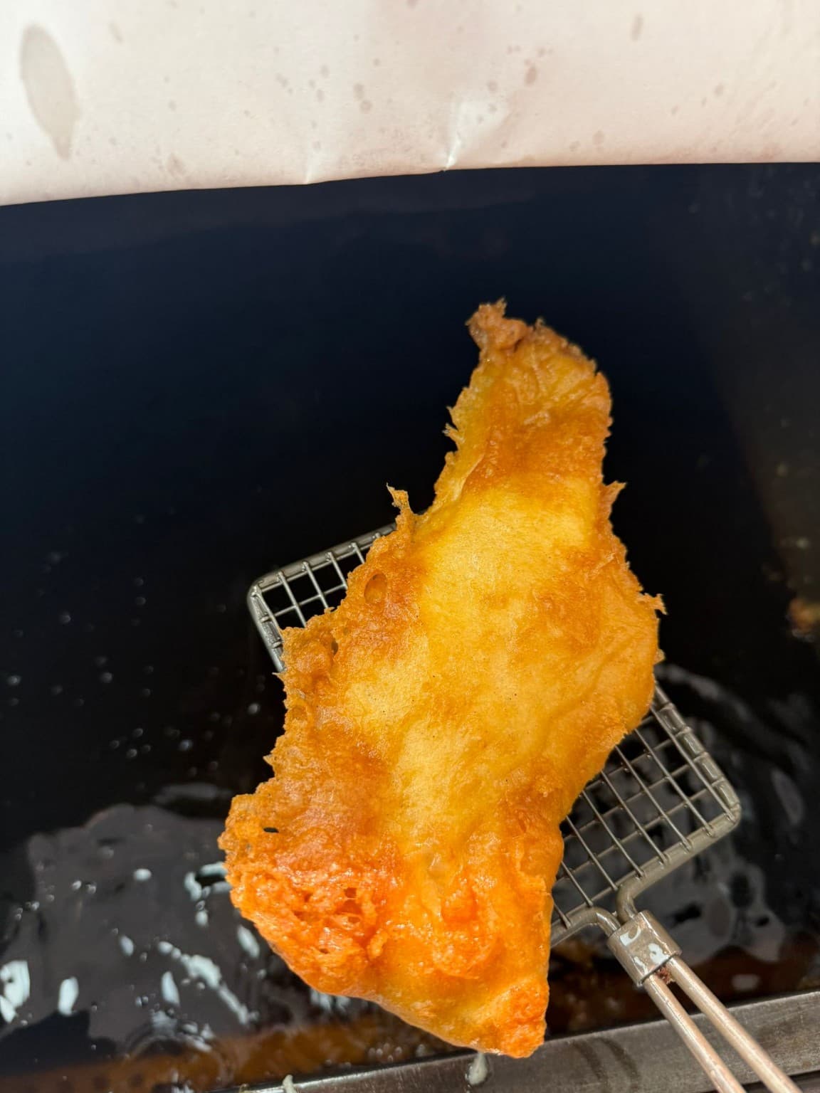 Freshly battered fish being lifted from the fryer